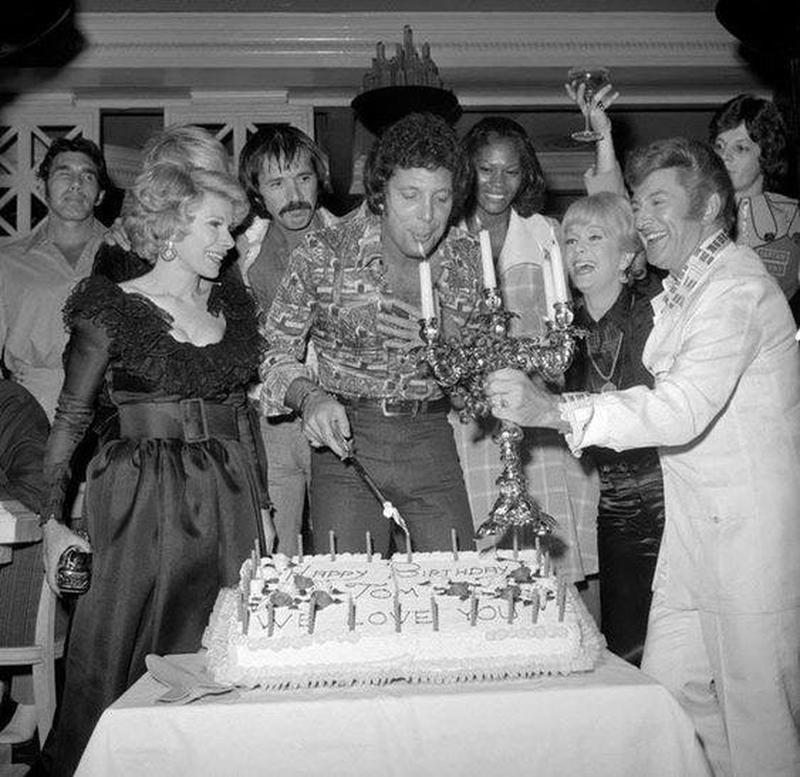 Celebrities join Singer Tom Jones in blowing out birthday candles at a surprise party held at Caesars Palace in 1974, with Joan Rivers, Sonny Bono, Dionne Warwick, Debbie Reynolds, and Liberace in attendance.