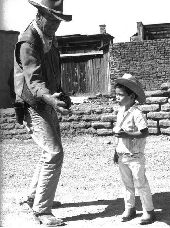 John Wayne showcases gun handling skills to his son on set during the 1950s.