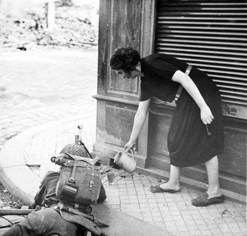 French woman shows kindness by serving hot tea to British soldier in Normandy, 1944.