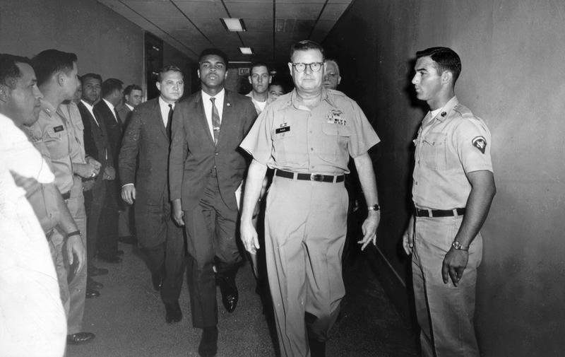 Muhammad Ali, heavyweight boxing champion, escorted from Houston's Armed Forces Examining and Entrance Station by Commandant Lt. Col. J. Edwin McKee following his refusal of Army induction in 1967.